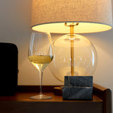 Atelier Chianti Red Wine Glass filled with white wine standing on a wooden table next to a table lamp