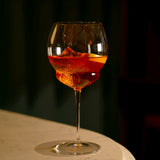 Backdoor '20s Gin & Tonic Cocktail Glass filled with Aperol Spritz cocktail and garnished with a blood orange slice standing on a marble surface and dark background