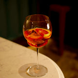 Backdoor '20s Gin & Tonic Cocktail Glass filled with Aperol Spritz cocktail and garnished with a blood orange slice standing on a marble surface and dark background