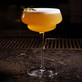 Backdoor '20s Great Gatsby Cocktail Glass filled with a yellow cocktail and garnished with yellow dry flowers, standing on a dark surface and dark background