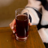 Hand holding Classico Highball Glass filled with pomegranate juice and standing on a wooden surface