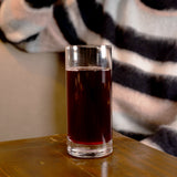Classico Highball Glass filled with pomegranate juice and standing on a wooden surface and a person with a striped sweater in the background
