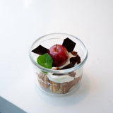 Lock-Eat Canning & Food Jar XL filled with an appetizing dessert of cream, cookies and finished with a miniature caramelized apple, chocolate chunks and a leaf, standing on a white surface