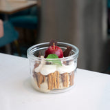 Lock-Eat Canning & Food Jar XL filled with an appetizing dessert of cream, cookies and finished with a miniature caramelized apple, chocolate chunks and a leaf, standing on a white surface