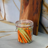 Lock-Eat jar filled with cut cucumbers and carrots standing on a marble surface with a wooden board in the background