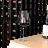 Talismano Italian Premium Bordeaux Red Wine Glass filled with a red wine standing on a wooden surface in a win cellar