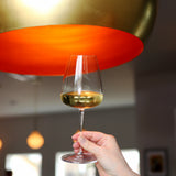 Hand holding a Talismano Chardonnay White Wine Glass filled with white wine on a orange and gold background