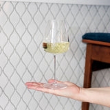 Talismano Chardonnay White Wine Glass filled with white wine standing on a flat hand on a white backsplash background