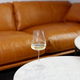Talismano Chardonnay White Wine Glass filed with white wine and standing on a white marble surface with a brown leather sofa in the background