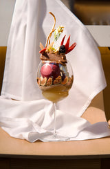 Gourmet dessert in a wine glass with decorative elements on a white cloth