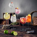 Six Gin and Tonic collection glasses filled with different color cocktails and standing on a wooden surface decorated with different cocktail garnishes