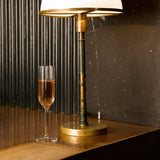 Bach flute filled with Rose wine standing on a wooden surface next to a table lamp on a dark background