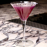 Bach Martini glass with a deep purple cocktail garnished with lavender standing on a black and white marble surface