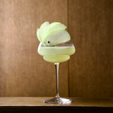 Backdoor '20s Great Gatsby Cocktail Glasses with a light green cocktail garnished with an apple standing on a wooden surface with a wooden wall in the background