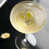 Top closeup of Backdoor '20s Nick & Nora Cocktail Glass filled with a clear light yellow cocktail and a blurred background