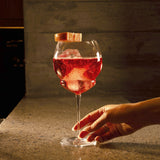 Hand holding a Backdoor '20s Gin & Tonic glass filled with Aperol Spritz on a marble surface and a dark background