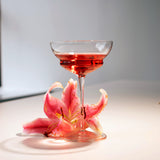 Backdoor '20s Hemmingway Special Cocktail Glass filled with clear red cocktail garnished with a pink lily on a light surface and background