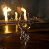 Empty Birrateque IPA Beer Glass standing on a wooden surface and a fireplace in the background