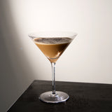 Crescendo Martini Glass filled with Espresso Martini cocktail standing on a dark wooden surface and a white background