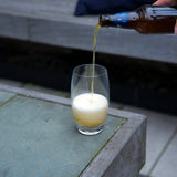 Beer being poured into a Crescendo Highball drinking glass standing on a wooden surface and blurred background
