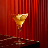 Cocktail garnished with a pear, in a Crescendo martini glass with a red wall background