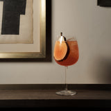Garnished with a pear slice red cocktail in a Gin & Tonic Jenever glass on a wooden surface with a framed picture in the background