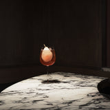 Cocktail in a Gin & Tonic Jenever glass with a pear twist on a marble surface against a dark background