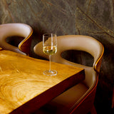 Grandioso Riesling glass filled with white wine standing on a wooden restaurant table with leather chairs in the background and a dark wall