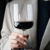 Hand holding a Grandioso Merlot glass filled with red wine a light blazer in the background