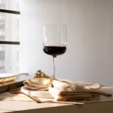 Grandioso Merlot glass filled with red wine standing on a set table with natural hues.