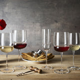 Grandioso glassware collection filled with red and white glasses standing on a wooden table with a vase and other décor in the background