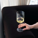 Hand holding a glass of white wine on a dark surface with a blurred background