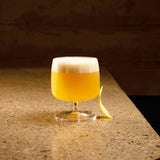 Jazz Rum Glass filled with a bright yellow cocktail and garnished with a lemon peel in the side of the glass, standing on a marble surface and dark background