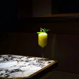 Jazz Negroni Cocktail Glass filled with bright green cocktail and garnished with mint leaves standing on a marble surface and a dark background