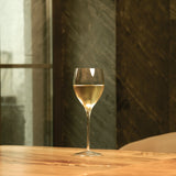 Magnifico medium wine glass filled with white wine standing on a wooden table and a dark green background