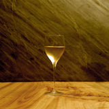 Magnifico medium wine glass filled with white wine standing on a wooden table and a dark background