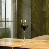 Magnifico large wine glass filled with red wine standing on a wooden table and a dark green background