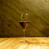 Magnifico large wine glass filled with red wine standing on a wooden table and a dark green background