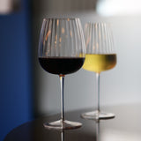 Gin & Tonic Jenever Gin glass filled with red wine standing on a dark surface, blurred white wine glass filled with white wine in the background