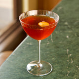Cocktail in a Optica Martini glass with an orange twist on a green marble surface