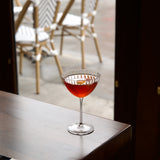 Cocktail in a Optica Martini glass on a bar with chairs and a window in the background