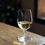 A clear Palace Water Goblet filled with white wine standing on a a wooden surface and a dark background