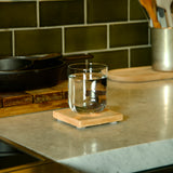 Sublime DOF glass filled with water standing on a coaster kitchen counter with various items in the background