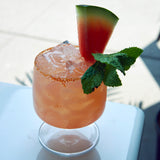 Sublime Cognac glass filled with a light red watermelon cocktail, garnished with mint and a watermelon slice, standing on a white surface