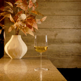 Sublime Brunello Di Montalcino red wine glass filled with white wine standing on a marble surface and a white vase with dry orange leaves in the background