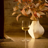 Sublime Brunello Di Montalcino red wine glass filled with white wine standing on a marble surface and a white vase with dry orange leaves in the background