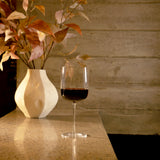 Sublime Barolo red wine glass filled with red wine standing on a marble surface and a white vase with dry orange leaves in the background