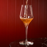 Supremo Chardonnay wine glass being filled with orange wine against a dark background