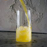 Top Class Highball Glass being filled with orange juice standing on a dark marble surface and light neutral textured background