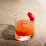 Veronese Whiskey Glass filled with orange cocktail and garnished with three cherries standing on a light surface